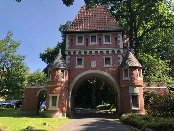 Speckenbütteler Park (c) Mailin Knoke (14).JPG Historisches Torhaus aus rotem Backstein mit spitzen Türmen, umgeben von grünen Bäumen im Gesundheitspark Speckenbüttel Bremerhaven.