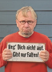 Bernd Stelter - Reg dich nicht auf Bernd Stelter mit ernster Miene hält ein Schild: „Reg' Dich nicht auf. Gibt nur Falten!“