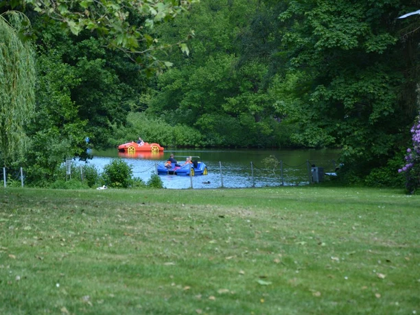bremerhaven_erlebnis_tretboot 07 (c) Andreas Larmann.jpg Menschen fahren in bunten Tretbooten über einen kleinen See, umgeben von dichtem grünen Bäumen.