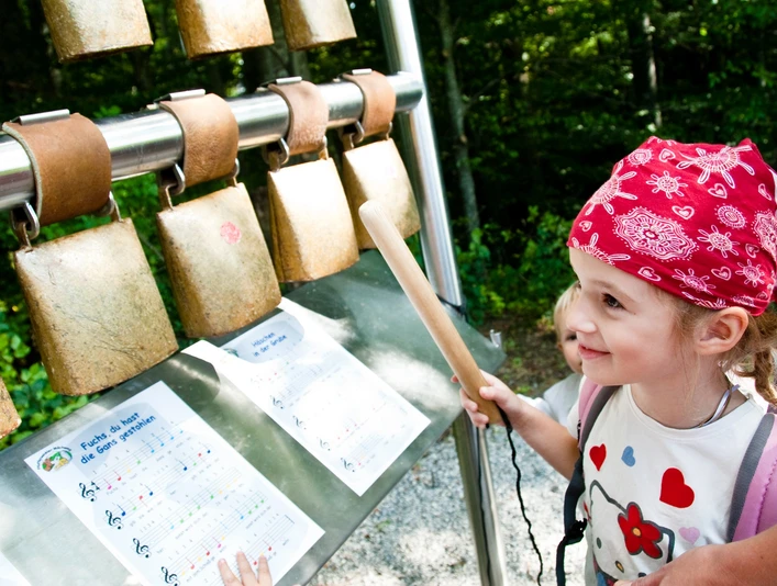 Schönegger Käse-Alm Ein Kind spielt mit Kuhglocken. Bunte Noten machen Gästen Freude.