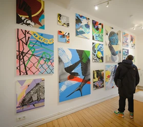 Fragmente-003 - Galerie Goethe45 Bilder des gebürtigen Bremerhaveners Dirk Mertin bestaunenn (c) Antje Schimanke Fotografie_Stadthalle Bremerhaven.jpg Person betrachtet farbenfrohe, abstrakte Gemälde mit Vögeln und Formen in einer hellen Galerie.