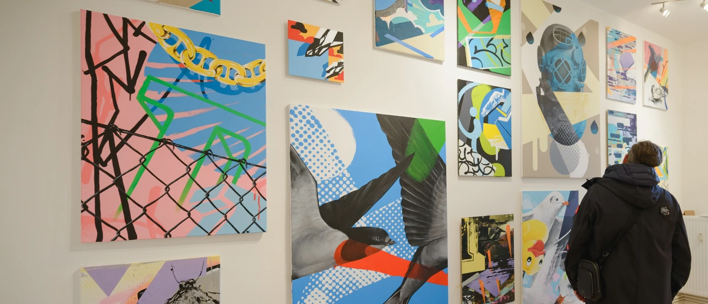 Fragmente-003 - Galerie Goethe45 Bilder des gebürtigen Bremerhaveners Dirk Mertin bestaunenn (c) Antje Schimanke Fotografie_Stadthalle Bremerhaven.jpg Person betrachtet farbenfrohe, abstrakte Gemälde mit Vögeln und Formen in einer hellen Galerie.