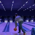 IMG_3693 (c) Lea Sophie Döscher_Erlebnis Bremerhaven1200x670.jpg Person beim Bowling in beleuchteter Halle, wirft orange Kugel auf leuchtende Pins unter blauem Licht.