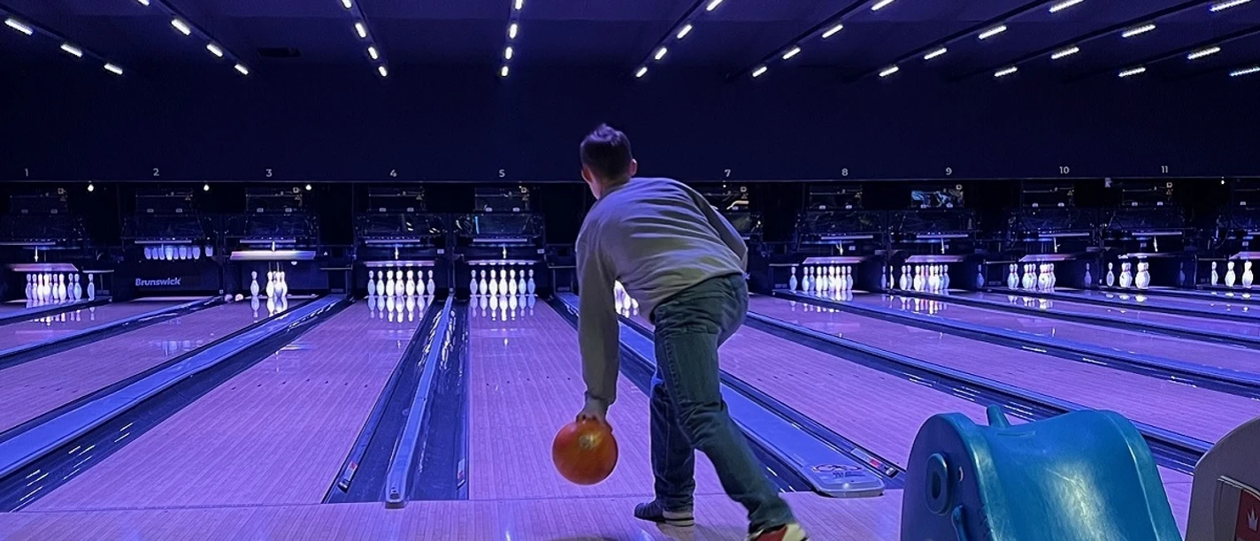 IMG_3693 (c) Lea Sophie Döscher_Erlebnis Bremerhaven1200x670.jpg Person beim Bowling in beleuchteter Halle, wirft orange Kugel auf leuchtende Pins unter blauem Licht.