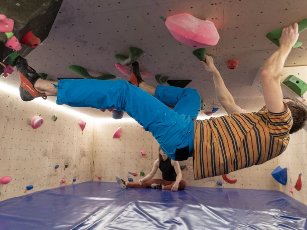 IMG_9300 (c) Hannes Voigts_Erlebnis Bremerhaven.jpg Person beim Bouldern an überhängender Kletterwand mit bunten Griffen in der Halle.