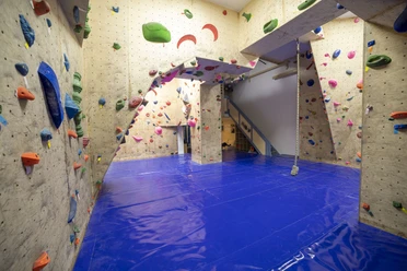 IMG_9329 (c) Hannes Voigts_Erlebnis Bremerhaven.jpg Innenraum einer Kletterhalle mit bunten Griffen, blauen Matten und Seil zum Training an der Wand.