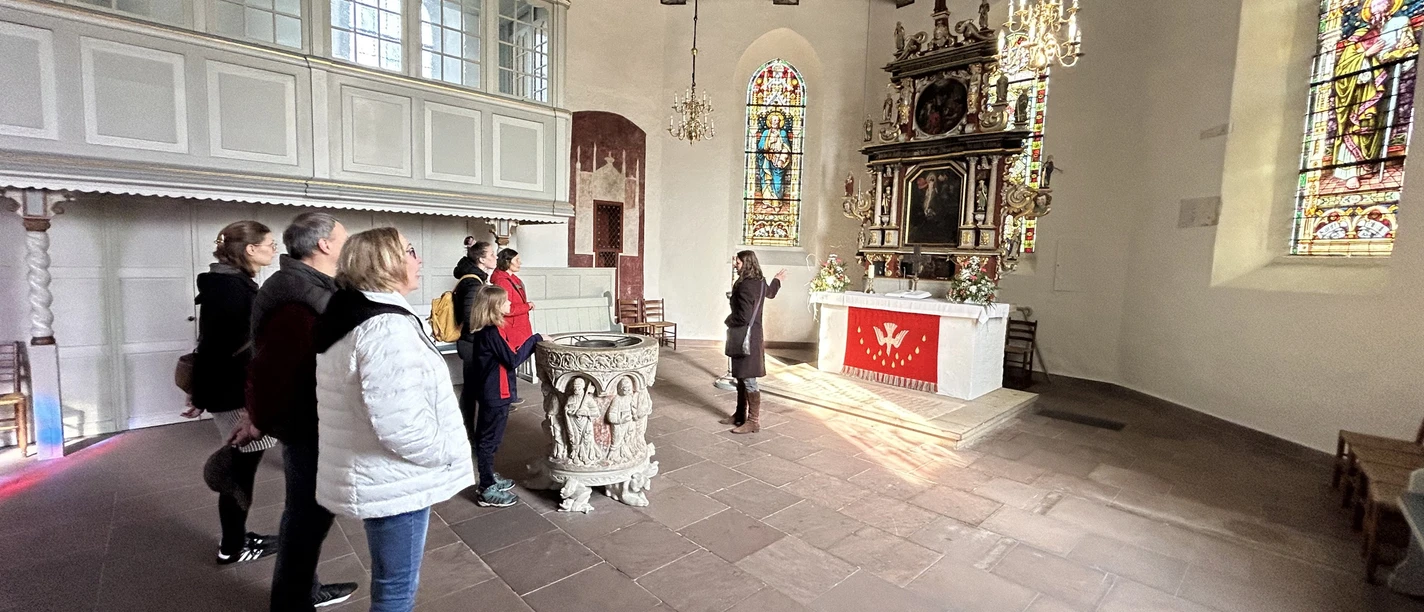 Gästeführung vor dem Altar der Kirche Gruppe in der St.-Ulrichs-Kirche betrachtet den Altarraum mit bunt leuchtenden Kirchenfenstern.