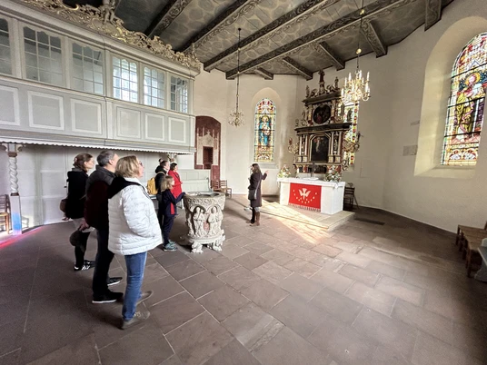 Gästeführung vor dem Altar der Kirche Gruppe in der St.-Ulrichs-Kirche betrachtet den Altarraum mit bunt leuchtenden Kirchenfenstern.