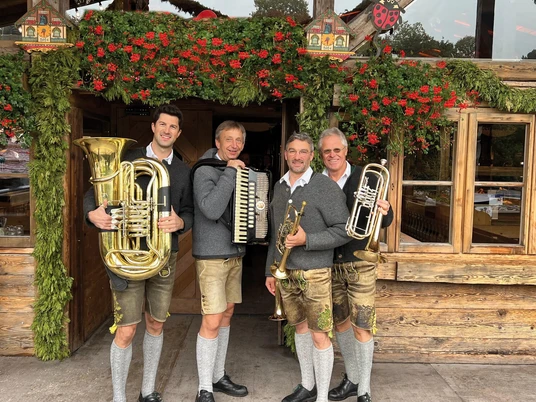 Hinterberger-Musikanten-2026.jpg Vier Hinterberger Musikanten in Tracht vor festlicher Almhütte