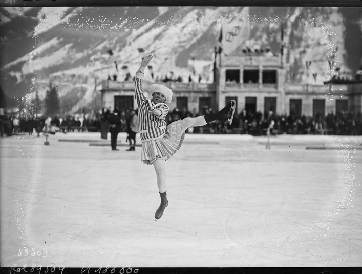 Sonja Henie at the Winter Olympics Eiskunstläuferin springt vor winterlicher Bergkulisse auf einer großen Freiluftbahn.Figure skater jumping in front of a wintry mountain backdrop on a large outdoor rink.