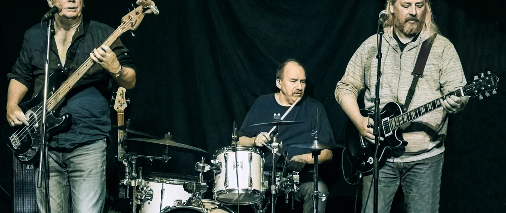 The Emerald Stars Apen Drei Musiker auf Bühne mit Bass, Schlagzeug und E-Gitarre während eines Live-Auftritts.