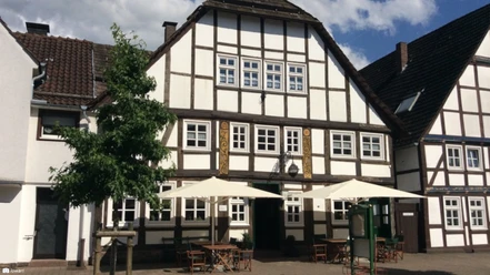 Stadtkrug Fachwerkhaus mit Außenbestuhlung und hellen Sonnenschirmen im Vordergrund.