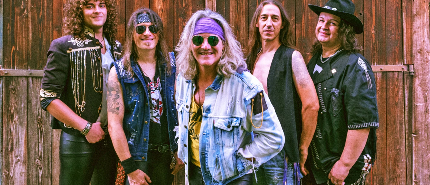 Bad Medicine Fünf Musiker in rockiger Kleidung posieren lächelnd vor einer Holzwand in lebendiger Bühnenatmosphäre.