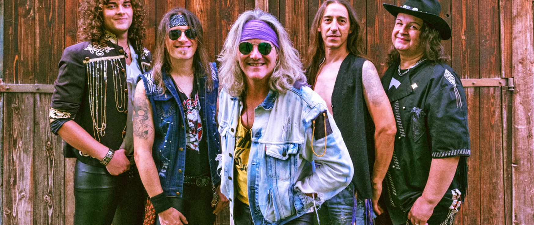 Bad Medicine Fünf Musiker in rockiger Kleidung posieren lächelnd vor einer Holzwand in lebendiger Bühnenatmosphäre.