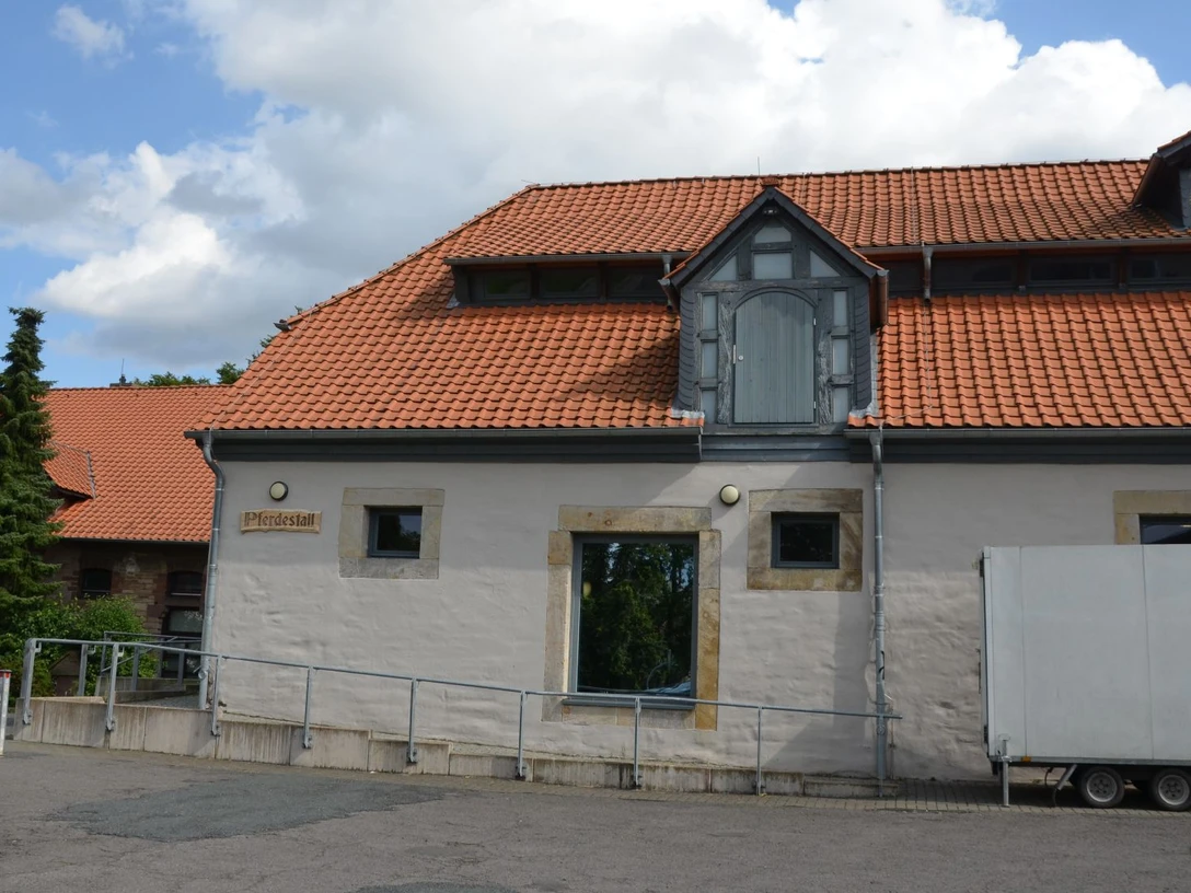 Pferdestall (3)_aussen_HD_16zu9.JPG Ehemaliger Pferdestall mit rotem Ziegeldach, heller Fassade und barrierefreier Rampe vor dem Eingang.