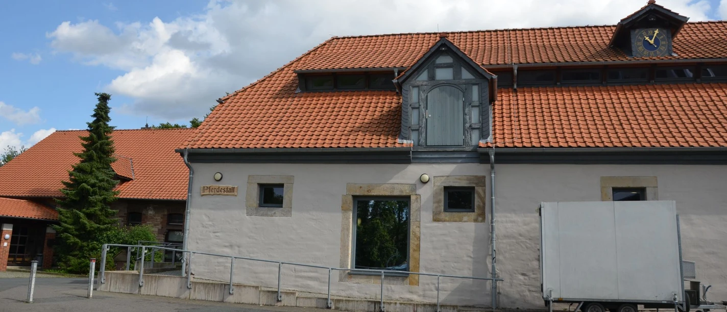 Pferdestall (3)_aussen_HD_16zu9.JPG Ehemaliger Pferdestall mit rotem Ziegeldach, heller Fassade und barrierefreier Rampe vor dem Eingang.