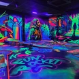 Leuchtende Schwarzlicht-Minigolfanlage mit bunten Graffiti-Wänden und futuristischer Atmosphäre