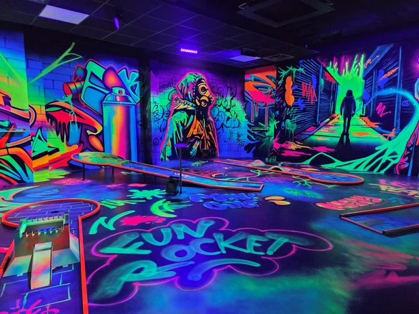 Leuchtende Schwarzlicht-Minigolfanlage mit bunten Graffiti-Wänden und futuristischer Atmosphäre