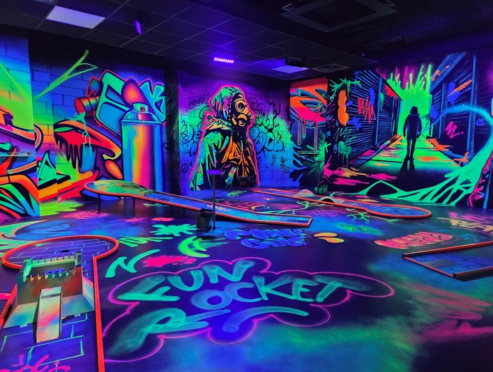 Leuchtende Schwarzlicht-Minigolfanlage mit bunten Graffiti-Wänden und futuristischer Atmosphäre