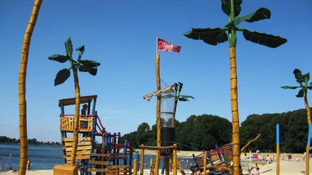 Großer Piratenspielplatz mit Holzschiff, Kletternetzen und Palmenfiguren am Sandstrand des Salzgittersees.