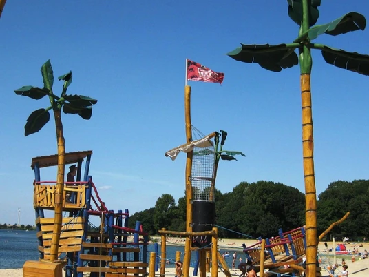 Piratenspielplatz19_HD_16zu9.jpg Großer Piratenspielplatz mit Holzschiff, Kletternetzen und Palmenfiguren am Sandstrand des Salzgittersees.