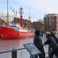 Feuerschiff-Deutsche Bucht.jpg Rotes Feuerschiff mit der Aufschrift »Deutsche Bucht« im Hafen, davor zwei bronzene Figuren an einem Geländer und eine Laterne.