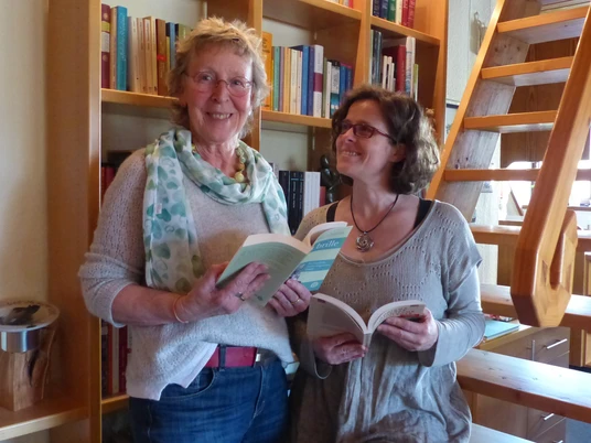 Lesung Schloss Benkhausen Zwei Frauen stehen vor Bücherregalen, halten Bücher und lesen auf einer Veranstaltung