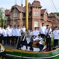 Shanty-Chor Overledinger Jungs Collinghorst.jpg Gruppe von Männern in weißen Matrosenhemden auf einem historischen Segelboot vor einem Backsteingebäude mit der Aufschrift 'FEHN- UND SCHIFFFAHRTSMUSEUM'