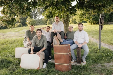 Strawanza.jpg Musikgruppe vor Reisekoffern unter Baum in weiter Natur