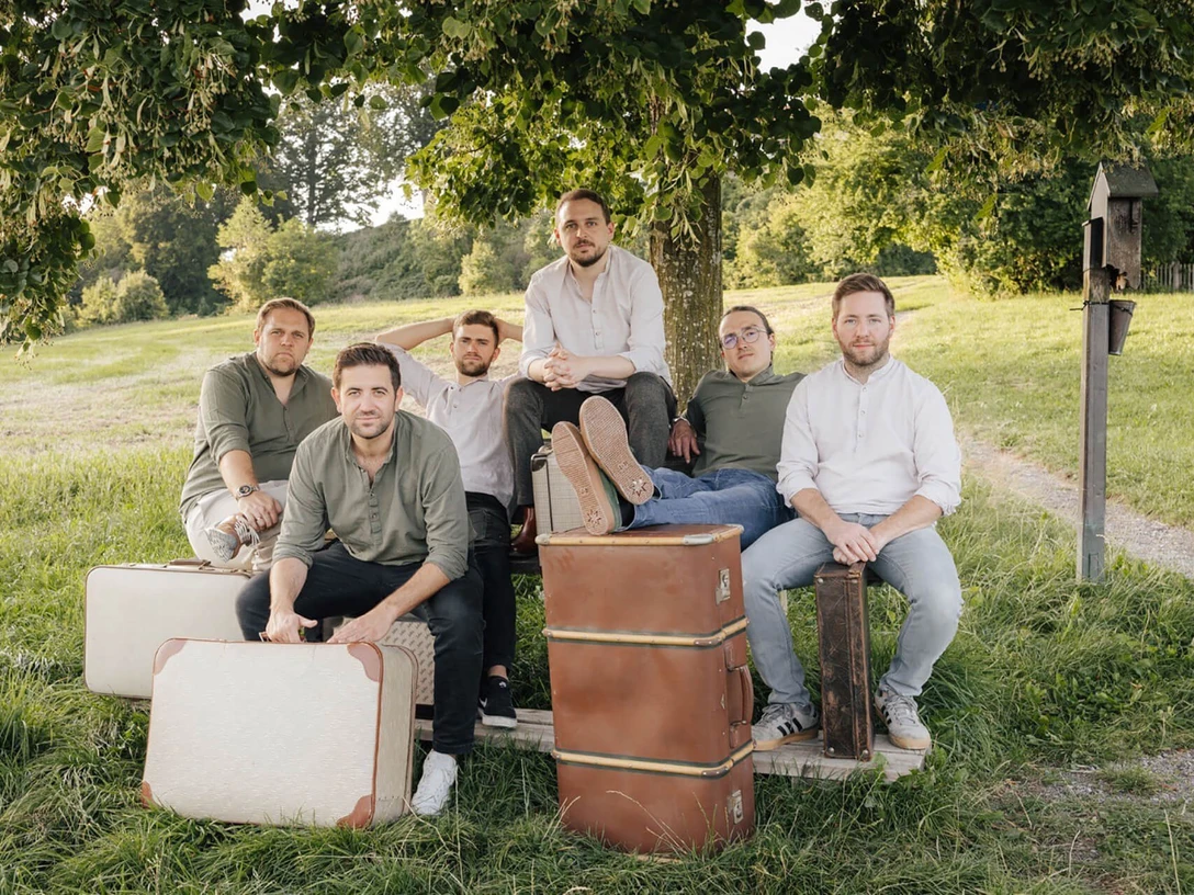 Strawanza.jpg Musikgruppe vor Reisekoffern unter Baum in weiter Natur