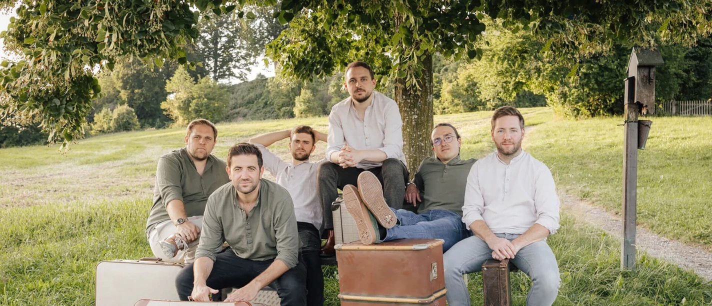 Strawanza.jpg Musikgruppe vor Reisekoffern unter Baum in weiter Natur