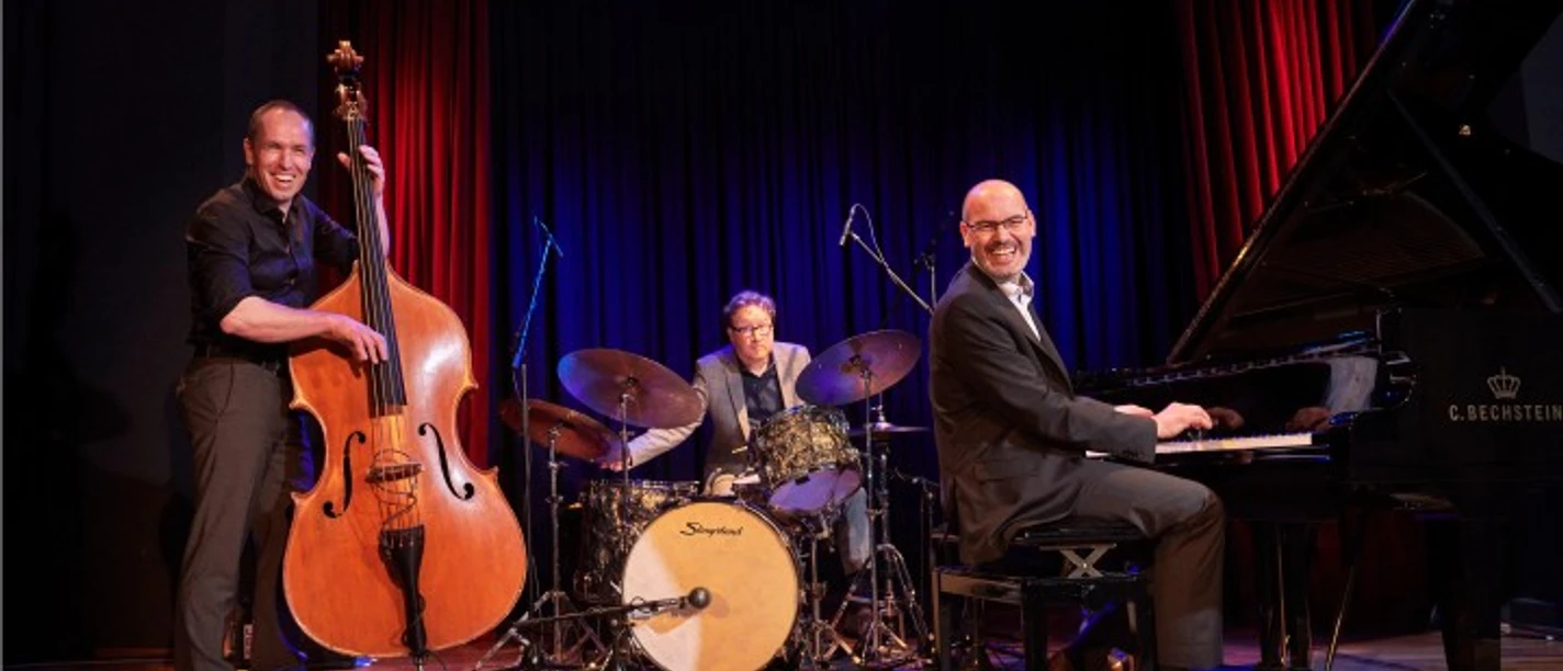 Frank Muschalle Trio Drei Musiker auf Bühne mit Kontrabass, Schlagzeug und Flügel bei Blueskonzert.
