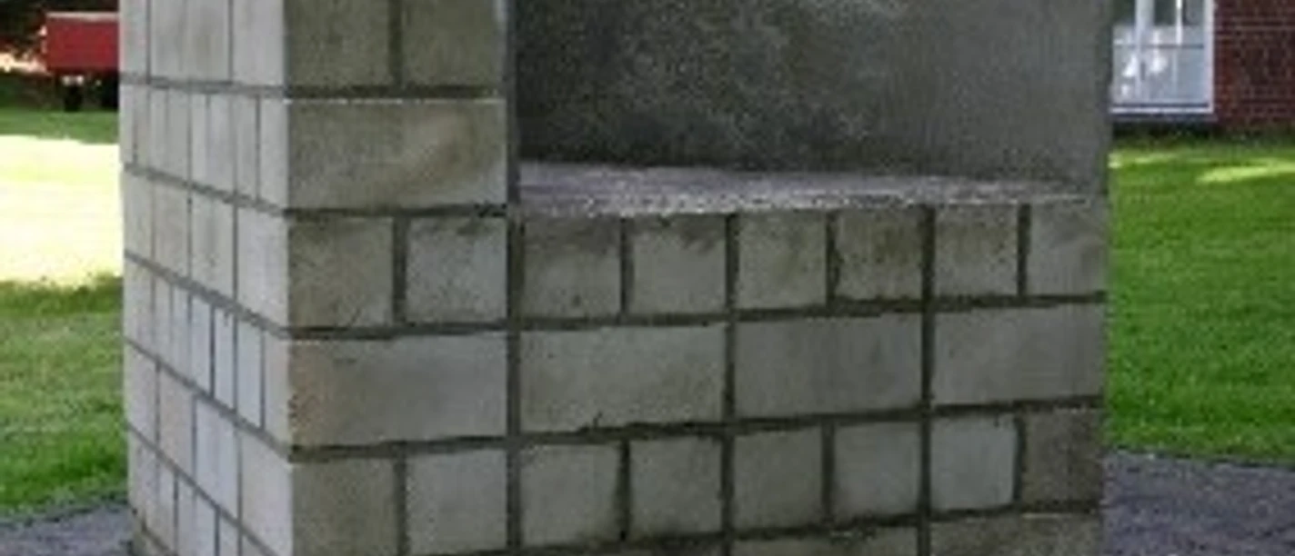 Skulpturen - Zwei gleichgroß Zweiteilige Betonskulptur aus grauen Quadern, modern platziert im Grünen vor einem Gebäude.