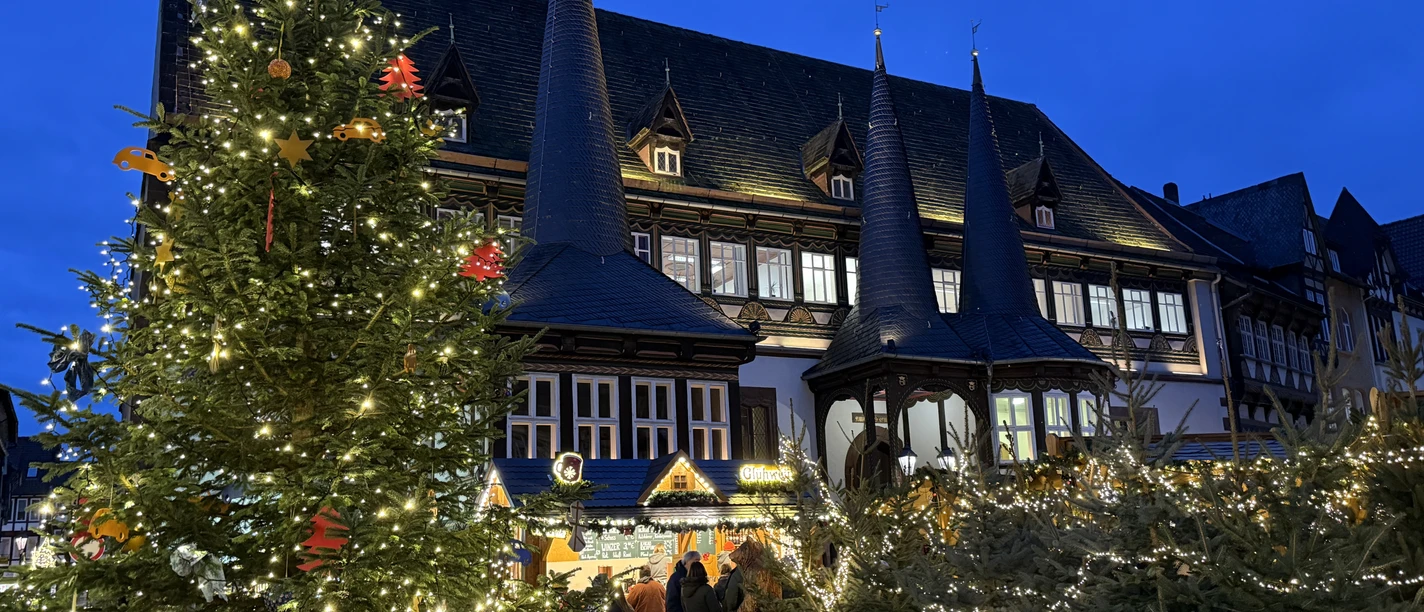 Einbecker Weihnachtsdorf Einbecker Rathaus mit beleuchtetem Weihnachtsbaum und Marktbuden in der Abenddämmerung.