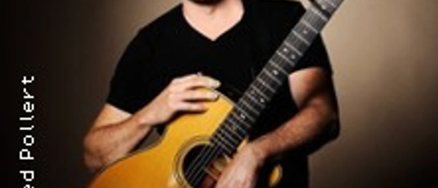 Ein lächelnder Mann hält eine Akustikgitarre vor neutralem Hintergrund in Porträtpose.