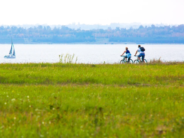 Zwenkauer See - Leipziger Neuseenland Blick auf den Zwenkauer See: ein Radfahrer fährt am Ufer entlang, während im Hintergrund ein Segelboot sanft über das Wasser gleitet.
