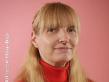 Frau mit blondem Haar in rotem Rollkragenpullover vor rosa Hintergrund.