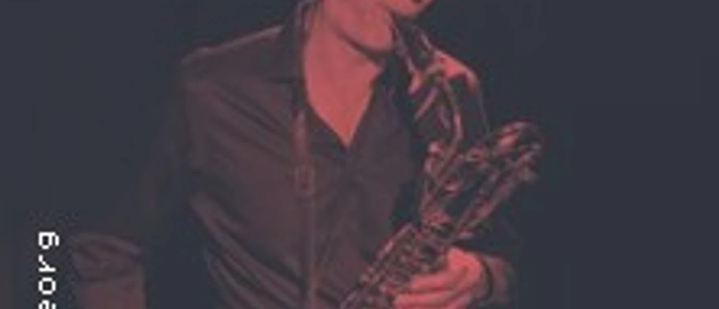 Saxophon spielende Person auf einer dunklen Bühne, ins rötliche Licht getaucht.