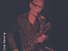 Saxophon spielende Person auf einer dunklen Bühne, ins rötliche Licht getaucht.