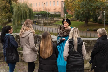 Stadtführung - Hann. Münden Marketing GmbH - Jules Stolzenhain-54.jpg Eine Frau in historischem Kostüm führt eine Gruppe auf einer Stadtführung im Freien an.