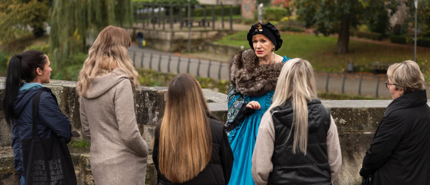Stadtführung - Hann. Münden Marketing GmbH - Jules Stolzenhain-54.jpg Eine Frau in historischem Kostüm führt eine Gruppe auf einer Stadtführung im Freien an.