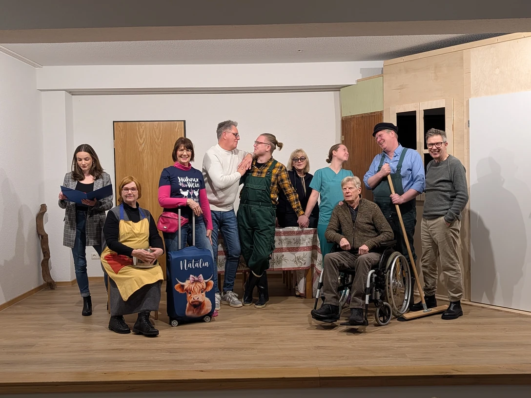 ''Ein Hof voller Narren'' Komödie von Winnie Abel Eine Theatergruppe steht auf einer Bühne, lacht und posiert in einer humorvollen Spielsituation.