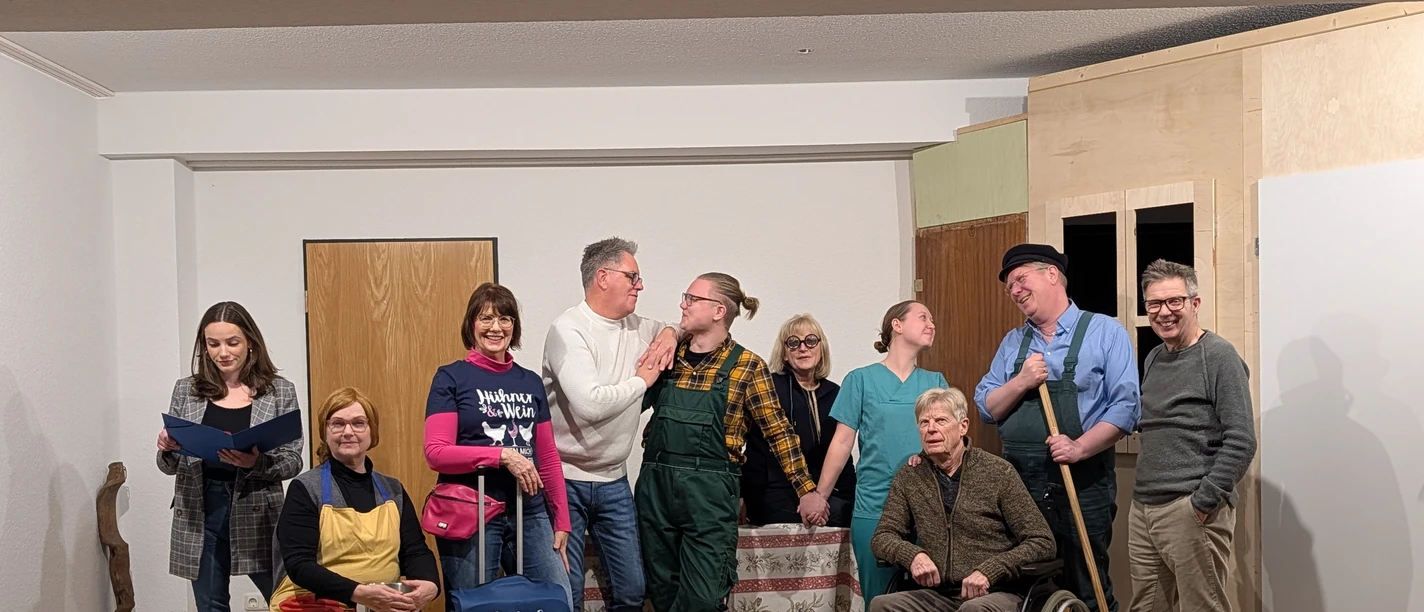 ''Ein Hof voller Narren'' Komödie von Winnie Abel Eine Theatergruppe steht auf einer Bühne, lacht und posiert in einer humorvollen Spielsituation.