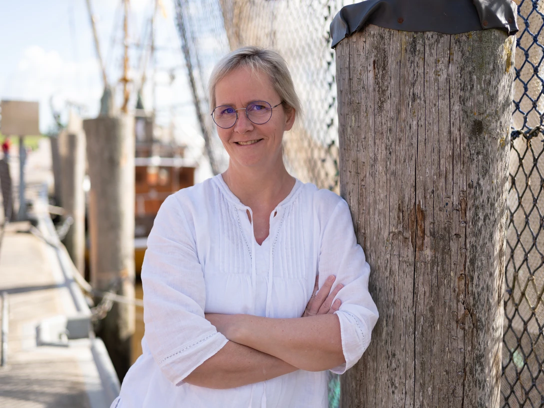 Elke Bergsma.jpg Frau in weißer Bluse lehnt mit verschränkten Armen an einem Holzpfahl im Freien