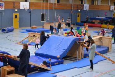 Action-Time in der Mehrzweckhalle Feldbreite Kinder und Erwachsene bewegen sich an Turngeräten und Matten in einer Sporthalle beim Turntraining.