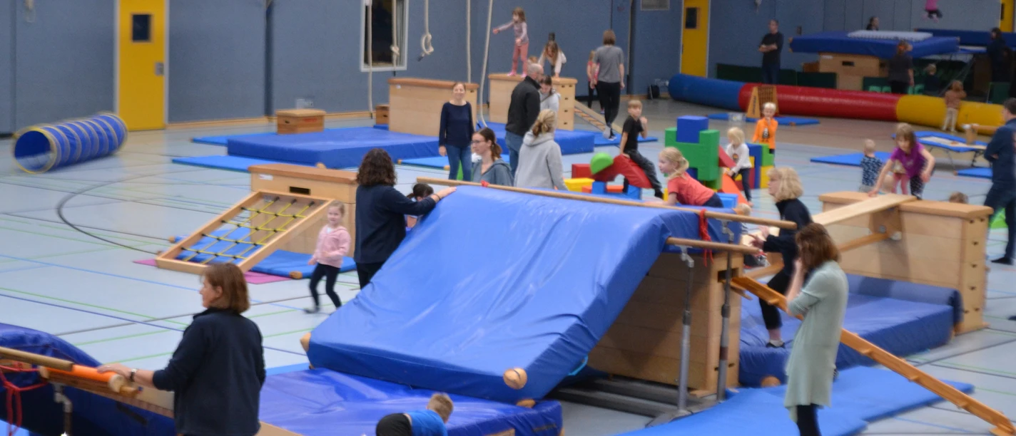 Action-Time in der Mehrzweckhalle Feldbreite Kinder und Erwachsene bewegen sich an Turngeräten und Matten in einer Sporthalle beim Turntraining.