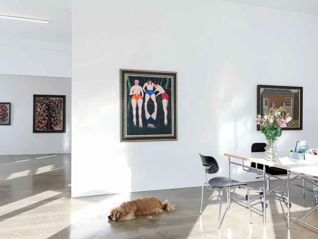 Sammlung Zander Köln Heller Galerieraum mit Gemälden, Arbeitstisch mit Blumen und ruhendem Hund am Boden.Bright gallery room with paintings, work table with flowers and resting dog on the floor.