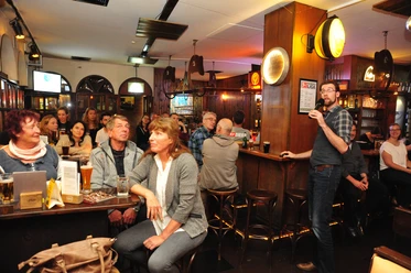Eine Gruppe hört in einer Bar einem Vortragenden mit Mikrofon aufmerksam zu.