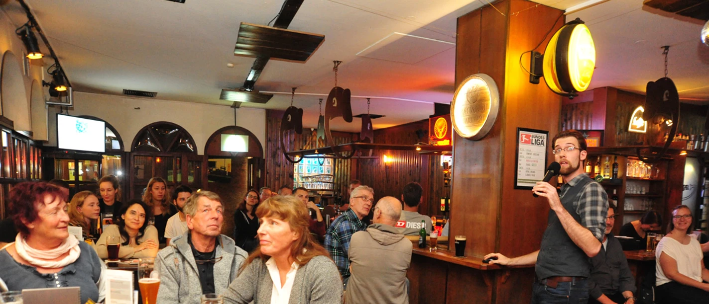 ScienceRüssel181018-013 (c) Jens Rillke_Erlebnis Bremerhaven.jpg Eine Gruppe hört in einer Bar einem Vortragenden mit Mikrofon aufmerksam zu.