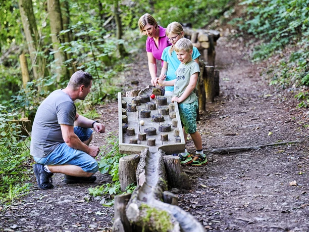 Die Waldkugelbahn gehört zu den Highlights für die Kleinen Gäste Ein Junge und ein Mädchen lassen ihre Kugel durch ein Element der Waldkugelbahn kullern. Die Eltern schauen zu.